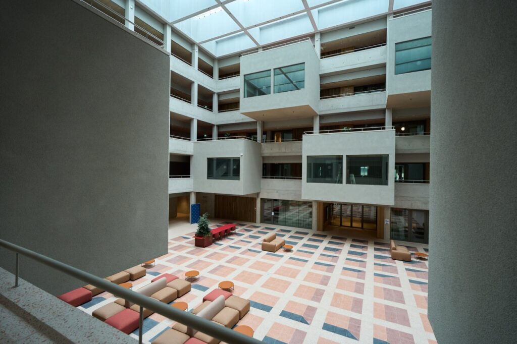 Nowoczesne wnętrze budynku z przestronnym atrium, wypełnionym kolorowymi sofami oraz dużymi oknami.