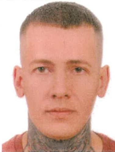 Mężczyzna z krótkimi włosami i tatuażami na szyi, patrzący w obiektyw aparatu.