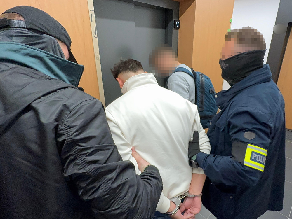 Mężczyzna w białej bluzie jest zatrzymywany przez dwóch policjantów w windy w nowoczesnym budynku.