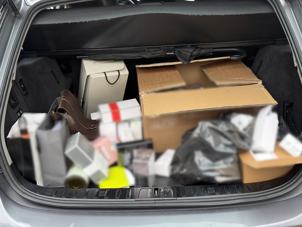 W bagażniku samochodu znajdują się liczne pakunki, w tym kartonowe pudła i torby, wypełnione różnymi przedmiotami.
