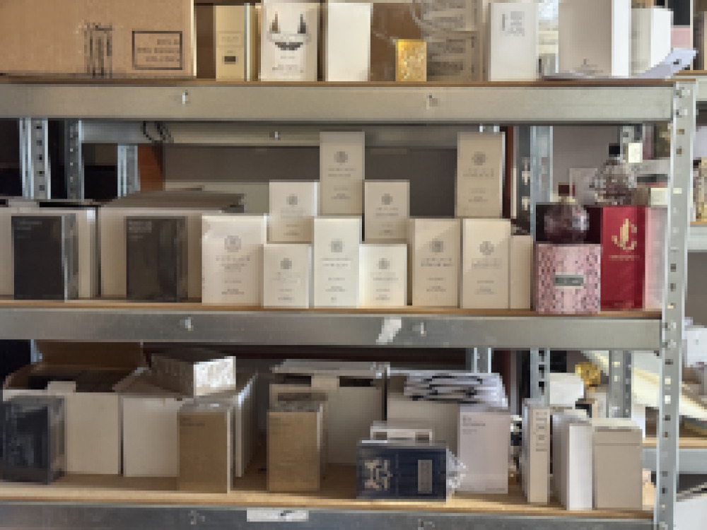 Półka z różnorodnymi opakowaniami perfum w jasnych i ciemnych kolorach, z widocznymi etykietami.