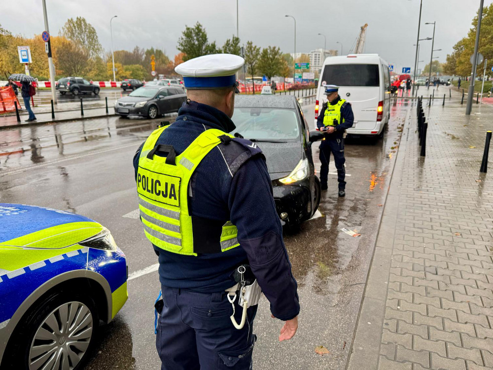Policjant w mundurze kontroluje kierowcę w deszczowym otoczeniu miejskim.
