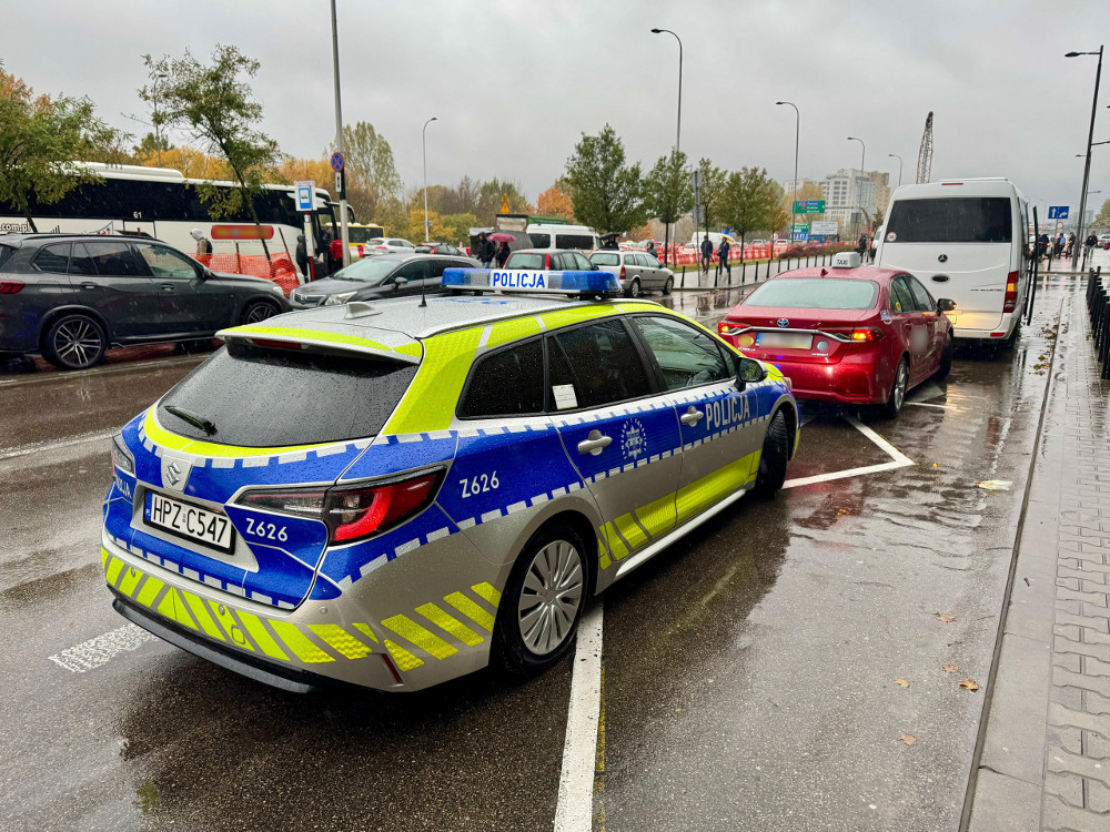 Policyjny samochód zaparkowany na ulicy, obok stojących pojazdów, w deszczowej aurze.
