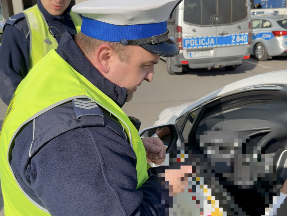 Policjant w kamizelce odblaskowej sprawdza dokumenty kierowcy w pojeździe na ruchliwej ulicy.