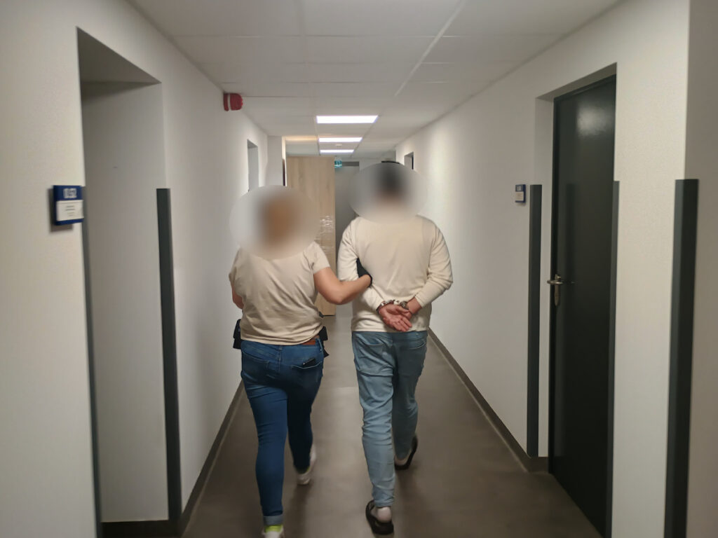 Mężczyzna i kobieta idą korytarzem w nowoczesnym budynku, trzymając się za ręce.