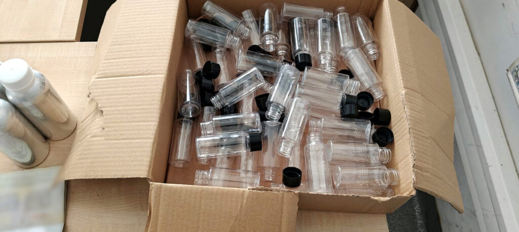 Pudełko z przezroczystymi butelkami plastikowymi i czarnymi zakrętkami, leżące na drewnianej powierzchni.