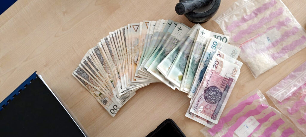 Stos pieniężny z banknotami o różnych nominałach leży na drewnianym stole obok woreczków strunowych.