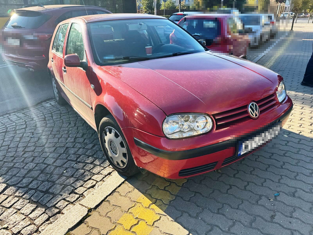Czerwony samochód osobowy marki Volkswagen zaparkowany na kostce brukowej w miejskim otoczeniu.