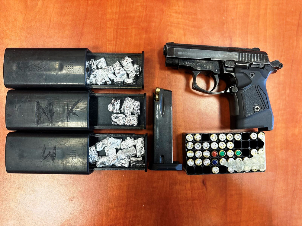 Pistolet leżący na drewnianym stole obok trzech czarnych pojemników z zawartością srebrnych folii oraz magazynka z amunicją.