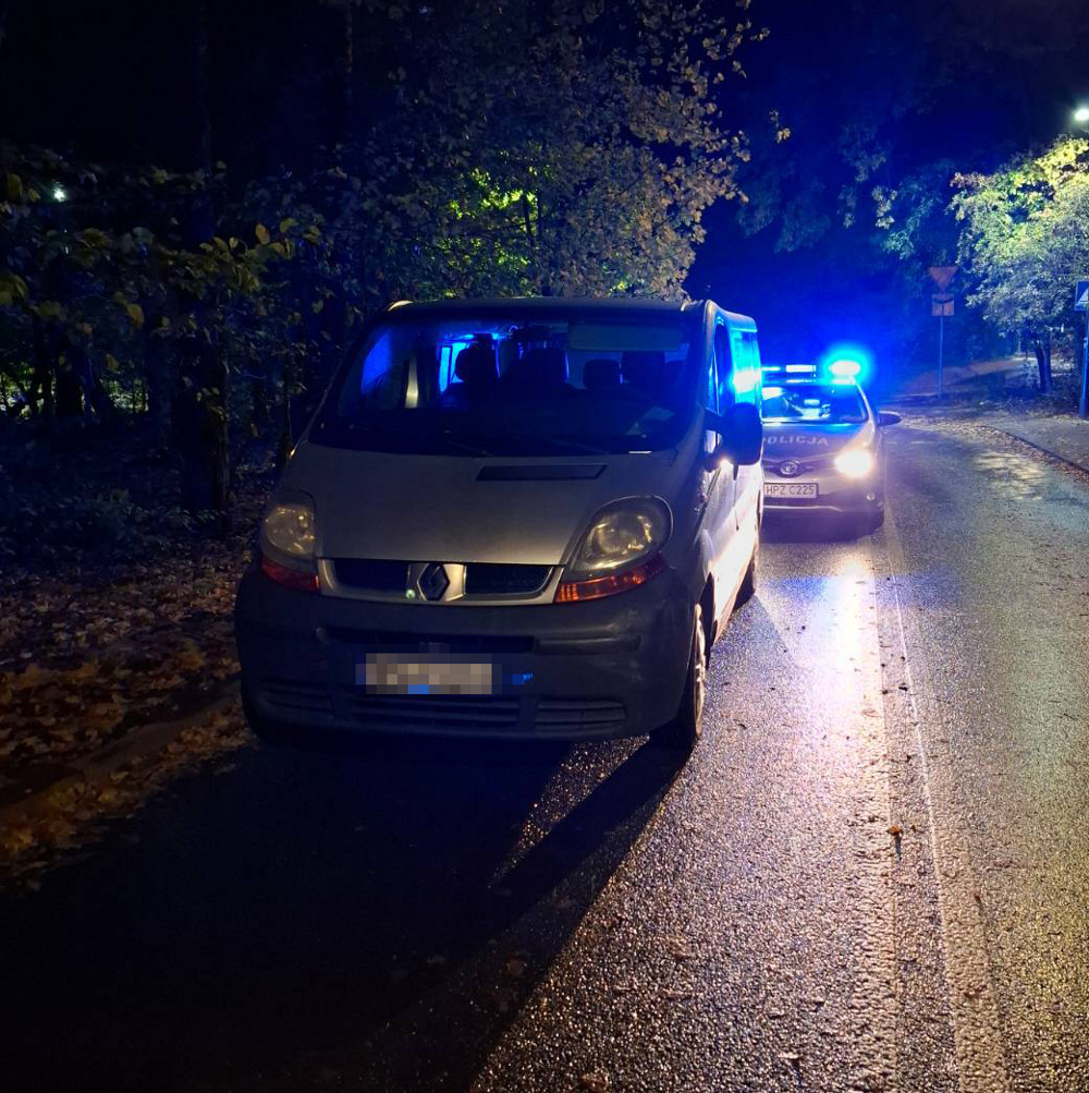 Renault stojący na poboczu drogi nocą, obok radiowóz z włączonymi niebieskimi światłami.
