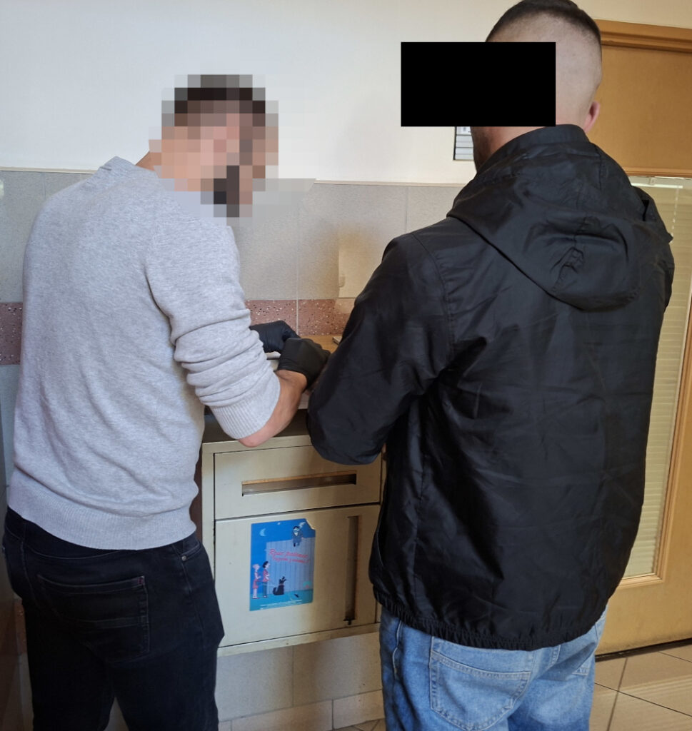Dwaj mężczyźni stoją przy metalowej skrzynce, jeden z nich trzyma przedmiot w rękach, drugi obserwuje.