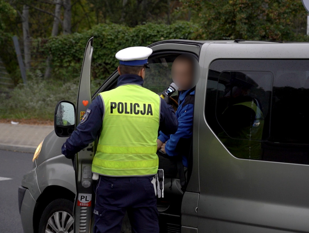 Policjant w kamizelce odblaskowej przeprowadza kontrolę drogową, sprawdzając kierowcę w samochodzie dostawczym.