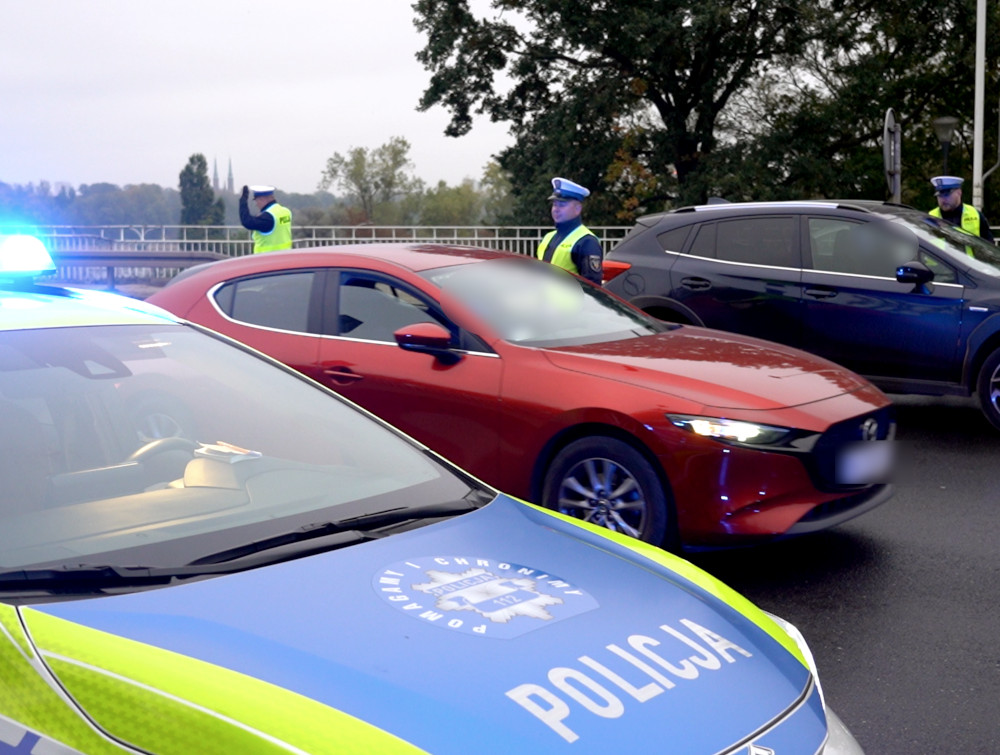 Policjanci w odblaskowych kamizelkach kierują ruchem drogowym przy zatrzymanych samochodach na ulicy.