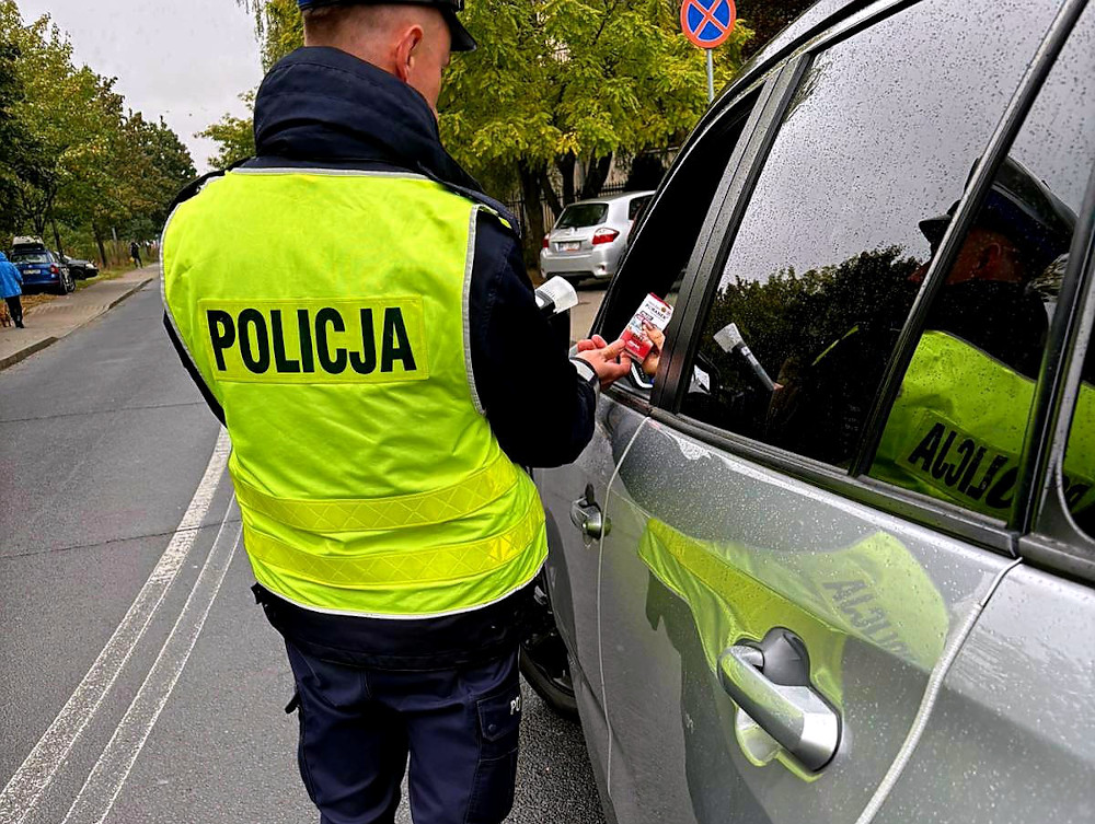 Policjant w odblaskowej kamizelce wręcza dokument kierowcy w samochodzie podczas kontroli drogowej.