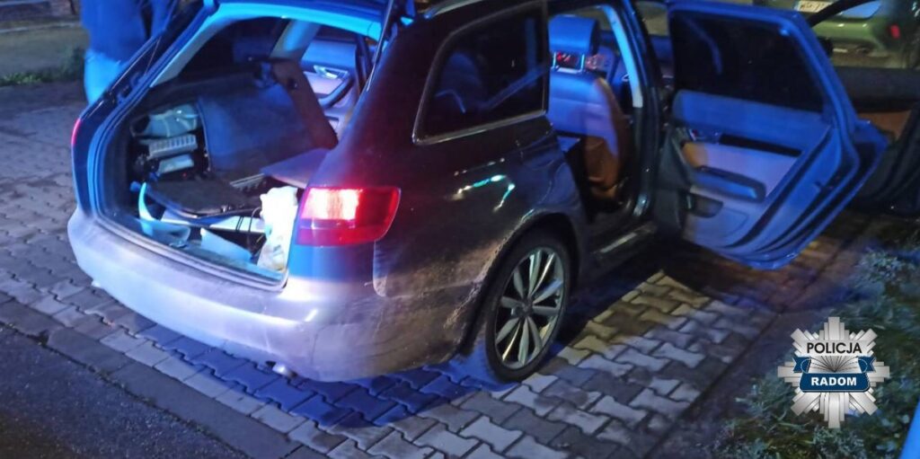 Otwarte tylne drzwi samochodu osobowego, w bagażniku widoczny sprzęt elektroniczny i inne przedmioty.
