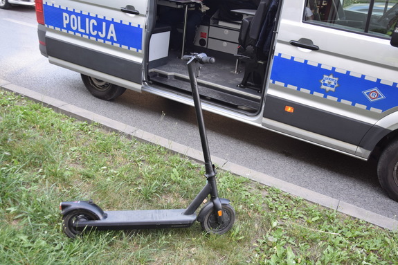 Czarna hulajnoga elektryczna stoi na trawie obok otwartego policyjnego furgonu.