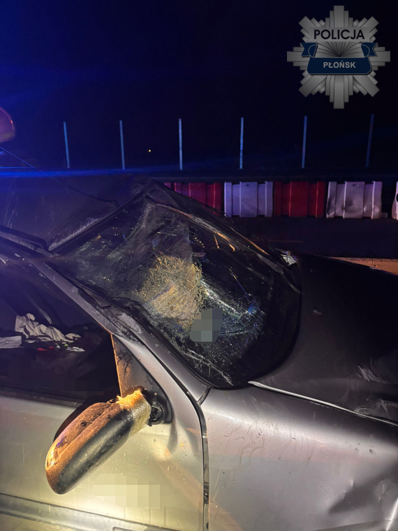 Zniszczony samochód osobowy z rozbitym przednią szybą, zaparkowany w nocy przy barierkach drogi.