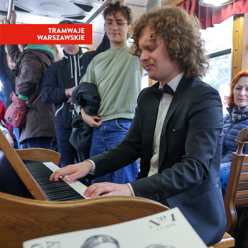 Mężczyzna w garniturze gra na pianinie w tramwaju, a pasażerowie słuchają i obserwują.