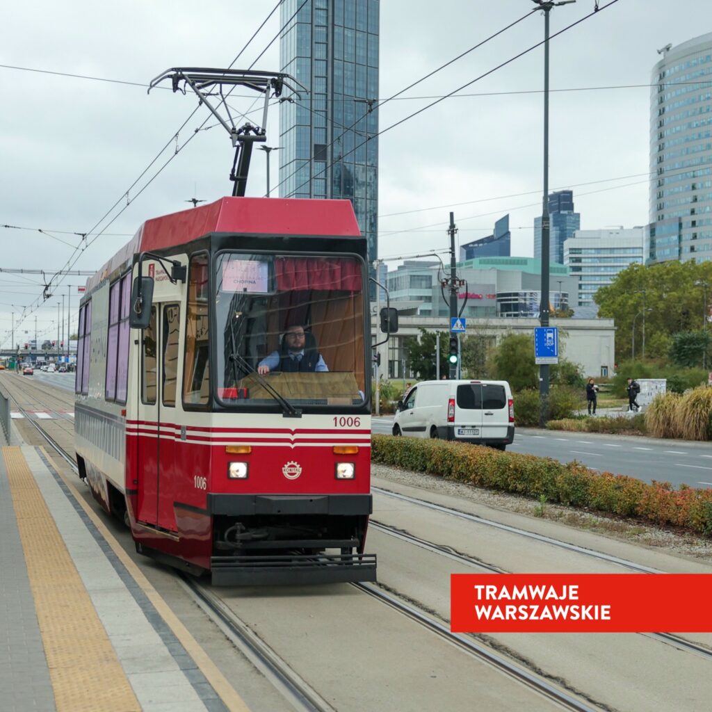 Tramwaj w czerwono-białym malowaniu przejeżdża po torach w miejskim krajobrazie, w tle nowoczesne wieżowce.