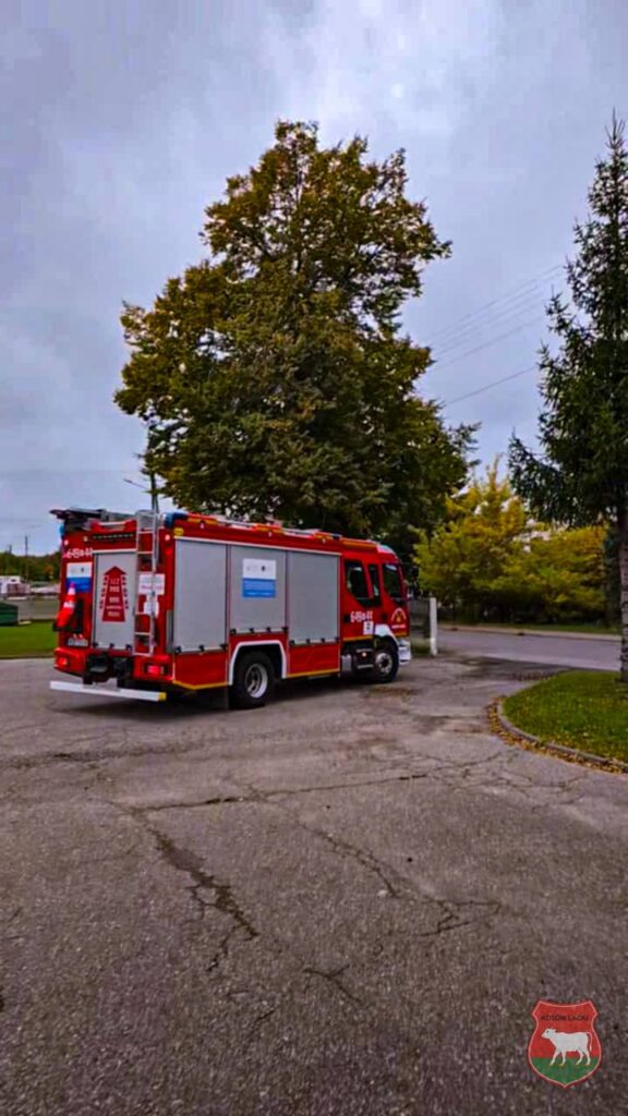 Czerwony wóz strażacki parkowany na asfaltowej drodze w otoczeniu drzew i zieleni.