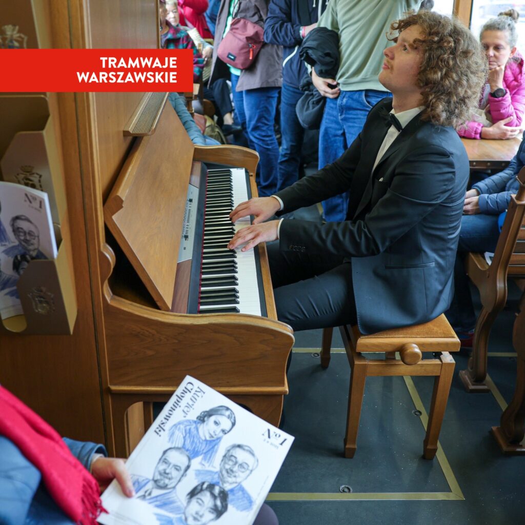 Mężczyzna w garniturze gra na pianinie w tramwaju, a pasażerowie słuchają i obserwują.