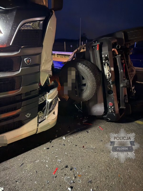 Ciężarówka z uszkodzoną przednią częścią stoi na drodze obok przewróconego pojazdu osobowego, na jezdni leżą fragmenty.