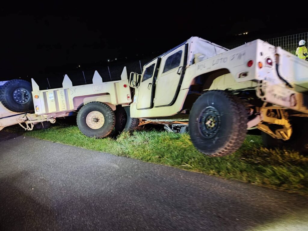 Złomowane pojazdy wojskowe leżą na poboczu drogi w nocy, obok zielonej trawy.