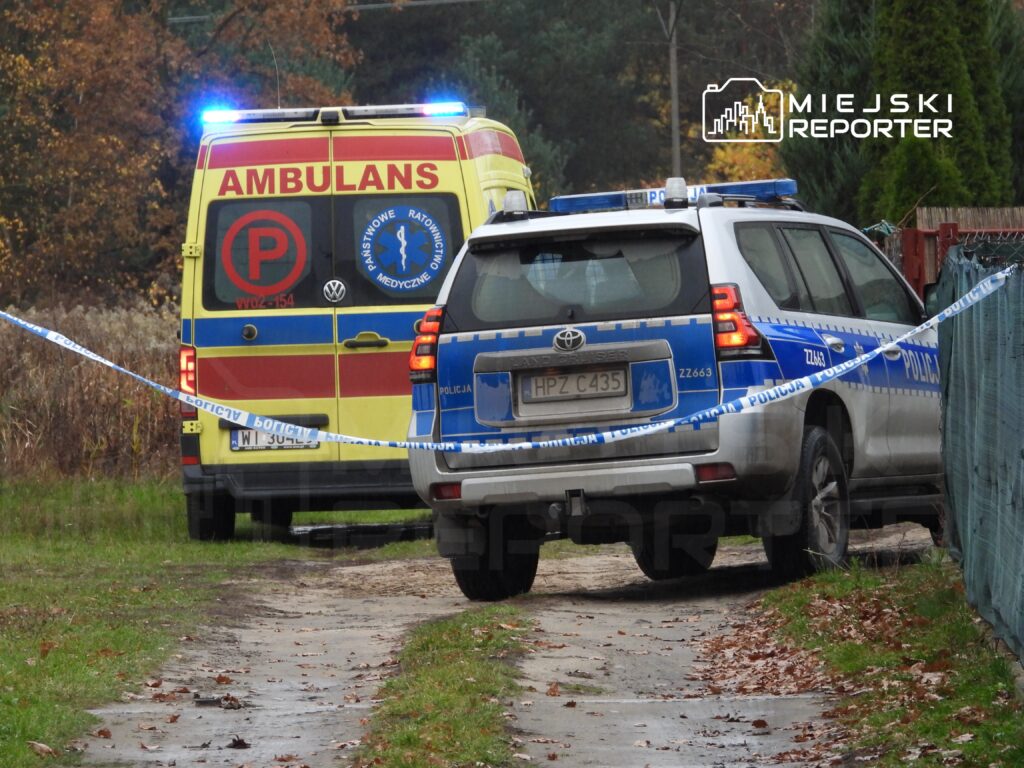 Karetka pogotowia i radiowóz policji stoją na leśnej drodze, oznaczone taśmą zabezpieczającą.