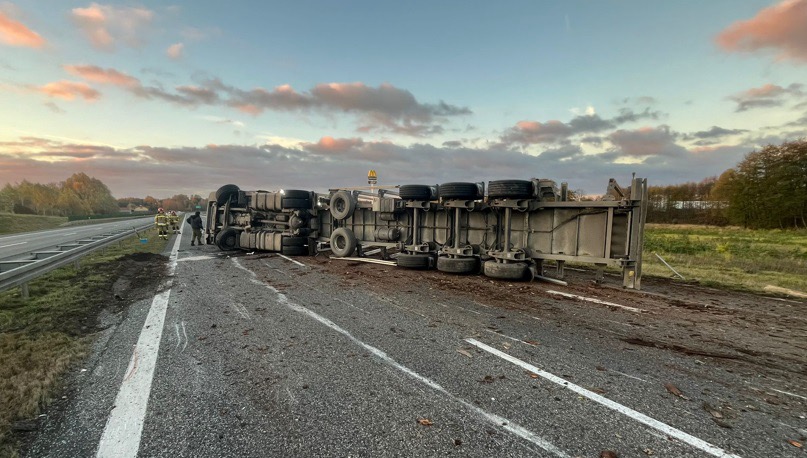 Cysterna leżąca na boku na drodze ekspresowej, obok pracownicy służb ratunkowych zabezpieczający miejsce zdarzenia.