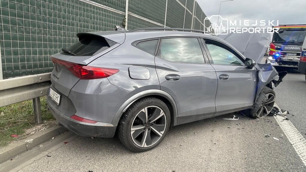 Uszkodzony samochód osobowy zaparkowany na poboczu drogi, obok widać ślady wypadku.