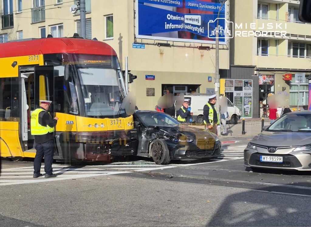 Zderzenie tramwaju z osobowym samochodem na skrzyżowaniu, obok funkcjonariusze policji zabezpieczający miejsce.