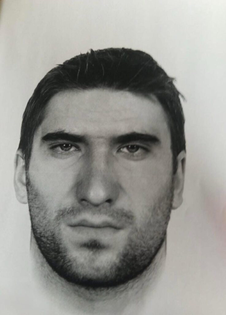 Mężczyzna o ciemnych włosach i zarostem patrzy prosto w obiektyw, na tle jasnego tła.