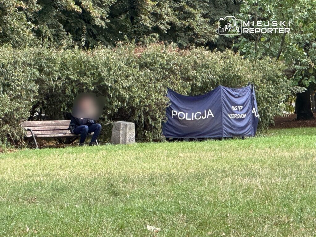 Mężczyzna siedzący na ławce obok policyjnego namiotu z napisem "WSTĘP ZABRONIONY" w parku.