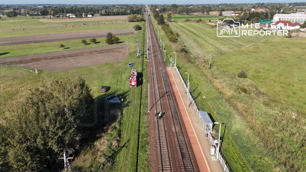 Na torach kolejowych stoją pracownicy w kamizelkach odblaskowych, obok widać straż pożarną oraz zaparkowane samochody.