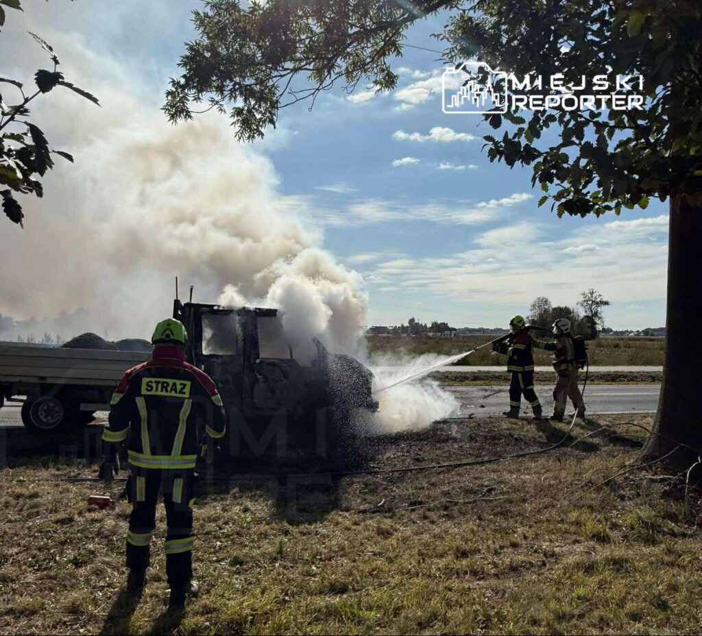 Strażacy gaszą pożar ciężarówki na poboczu drogi, z której wydobywa się gęsty dym.