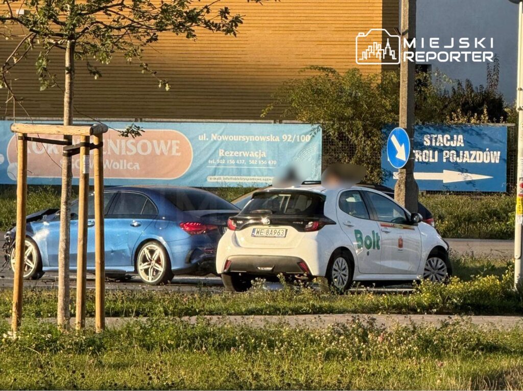 Dwa samochody zaparkowane obok siebie na ulicy, w tle widoczny billboard oraz znak kierunkowy.