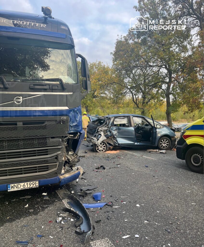 Wielka ciężarówka z uszkodzonym przodem stoi obok rozbitego samochodu osobowego, wokół leżą fragmenty karoserii.