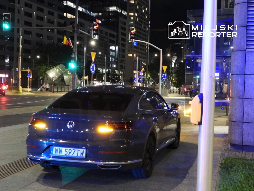 Czarny samochód marki Volkswagen Arteon zaparkowany na oświetlonej ulicy w nocy, w tle nowoczesne budynki.