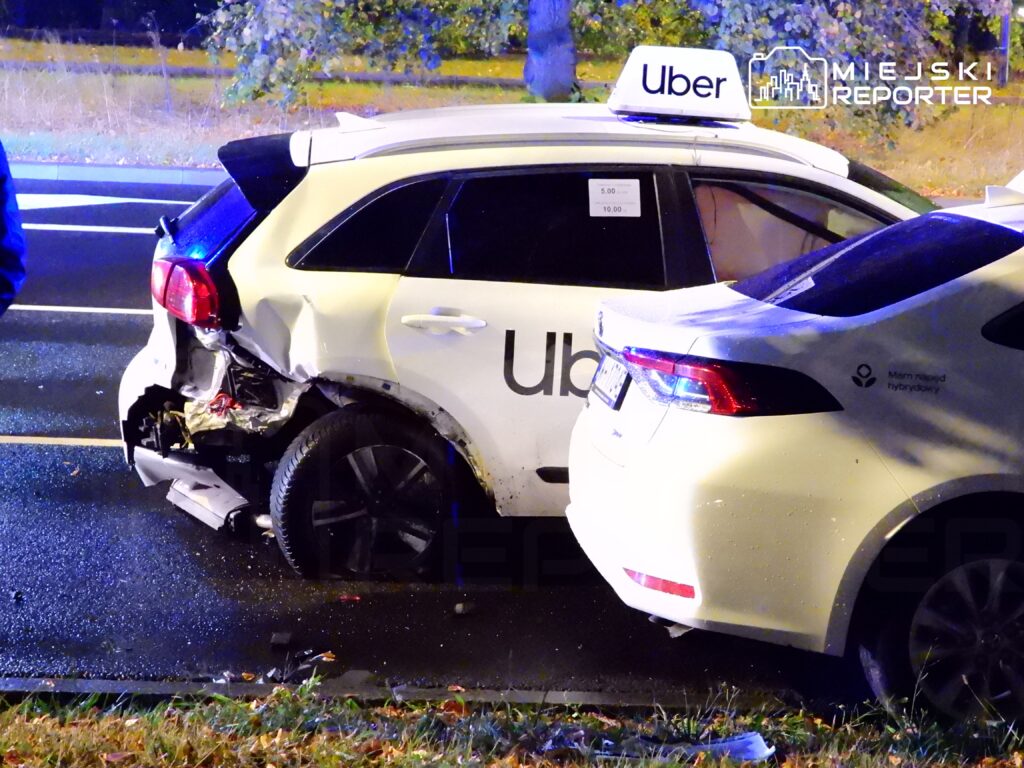 Dwa samochody osobowe z widocznymi uszkodzeniami stoją na drodze, obok policjant w niebieskiej kurtce.