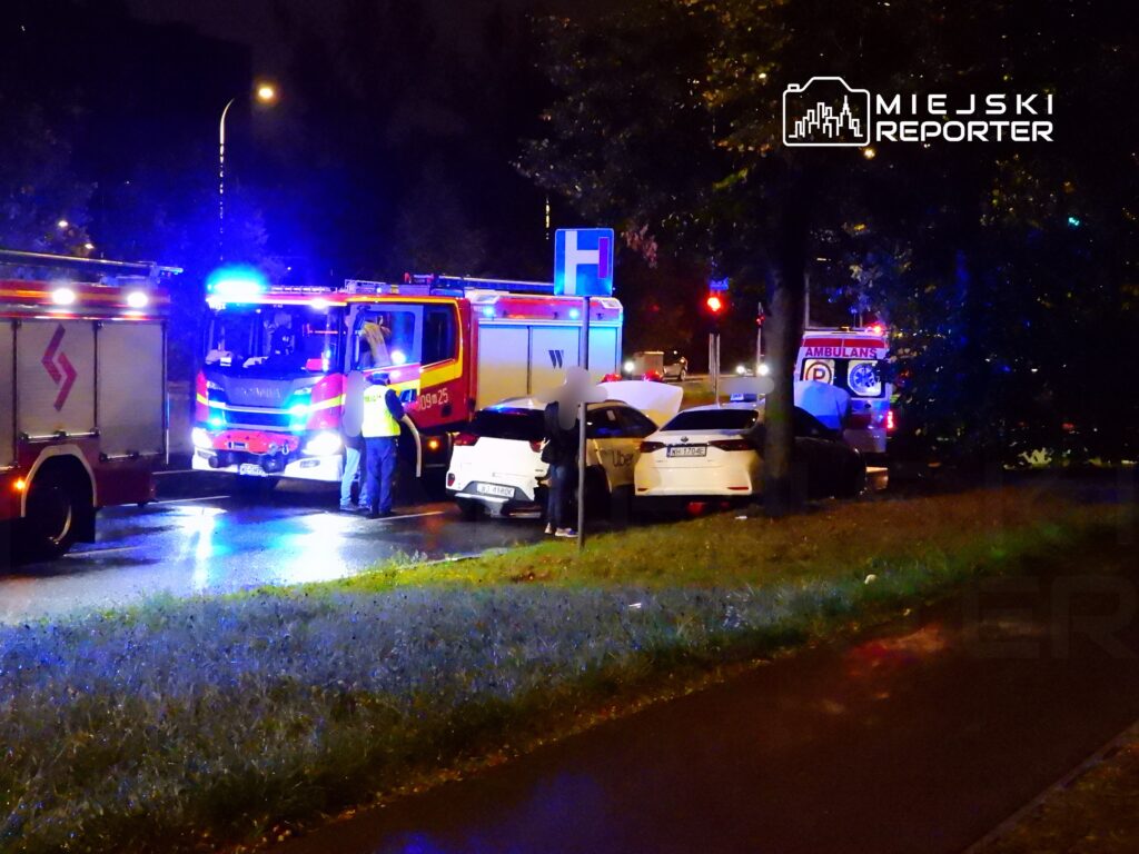 Strażacy z wozem ratunkowym zabezpieczają miejsce wypadku drogowego w nocy, obok uszkodzonych samochodów.