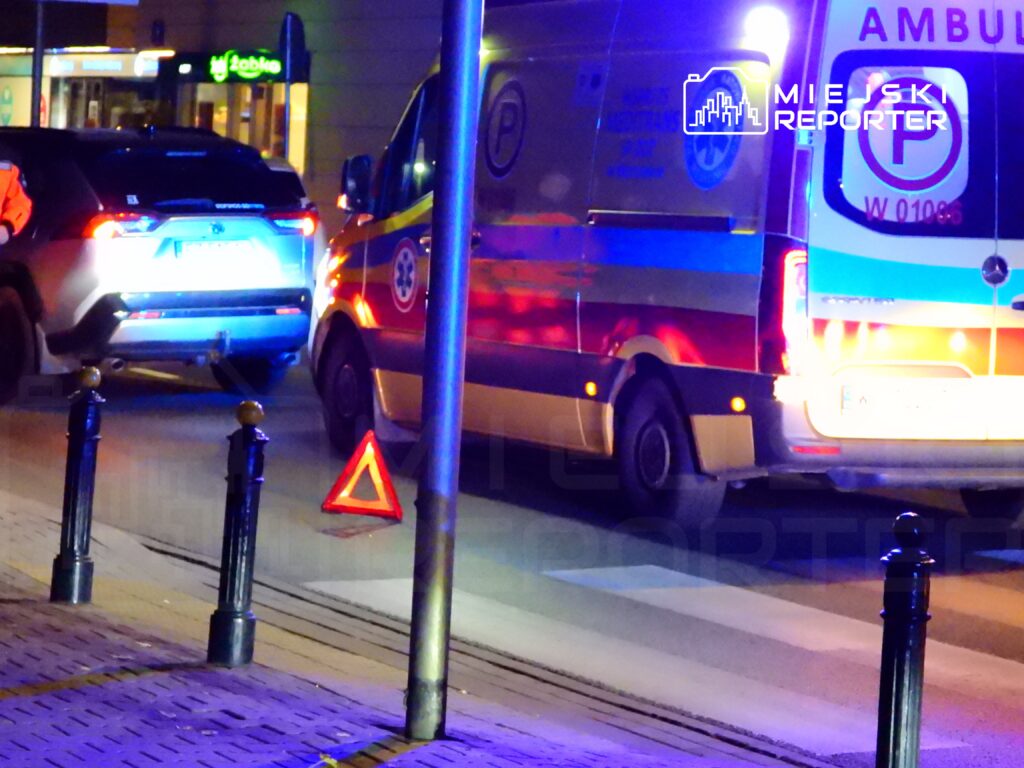 Kierowca SUV-a zatrzymany w nocy obok karetki pogotowia, na jezdni widoczny trójkąt ostrzegawczy.