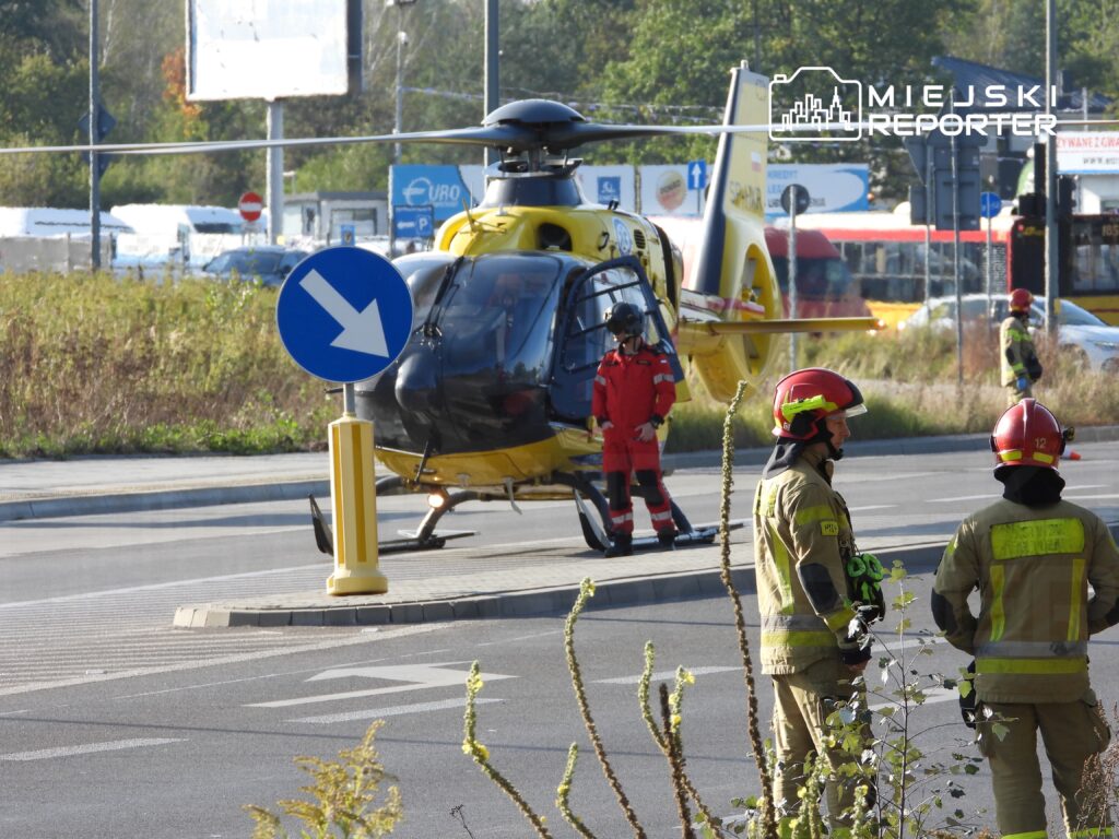 Helikopter ratunkowy ląduje na ulicy, obok grupy strażaków w mundurach i ratowników medycznych.