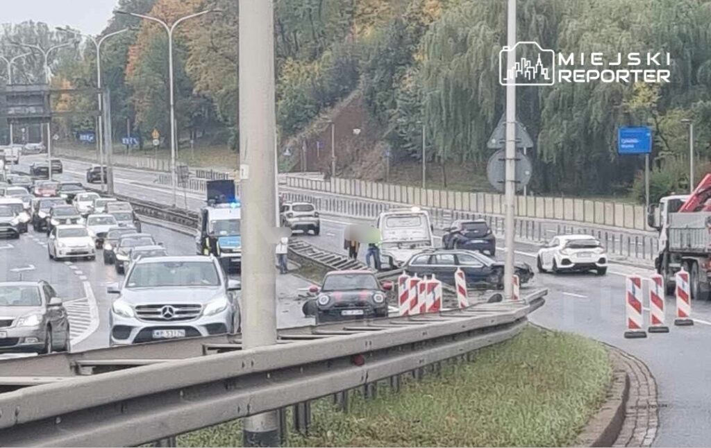Kilkanaście samochodów stojących w korku na drodze, z radiowozem i wozem strażackim na poboczu.