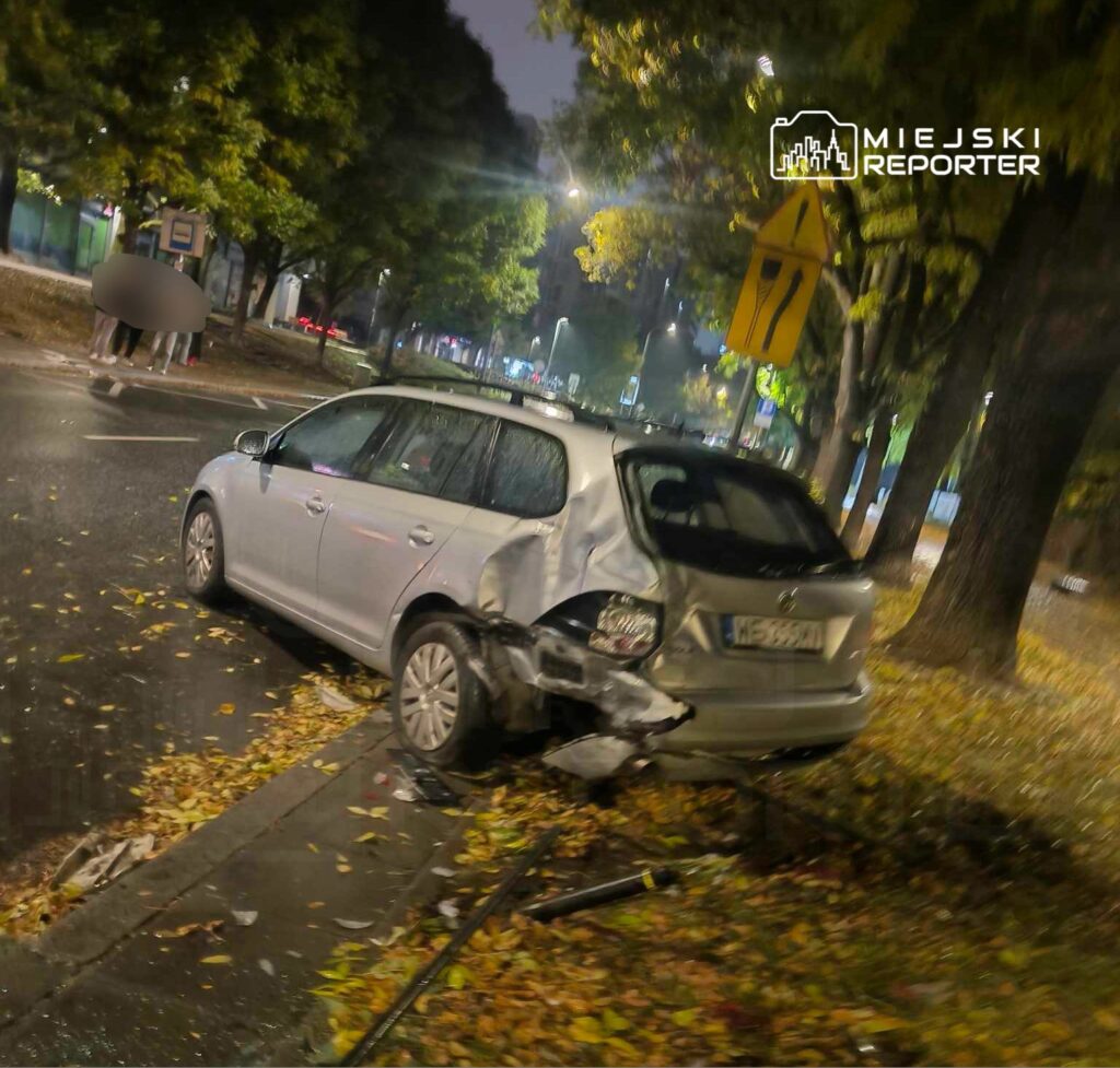 Uszkodzony samochód osobowy zaparkowany na chodniku, z widocznymi uszkodzeniami tyłu, otoczony opadłymi liśćmi.