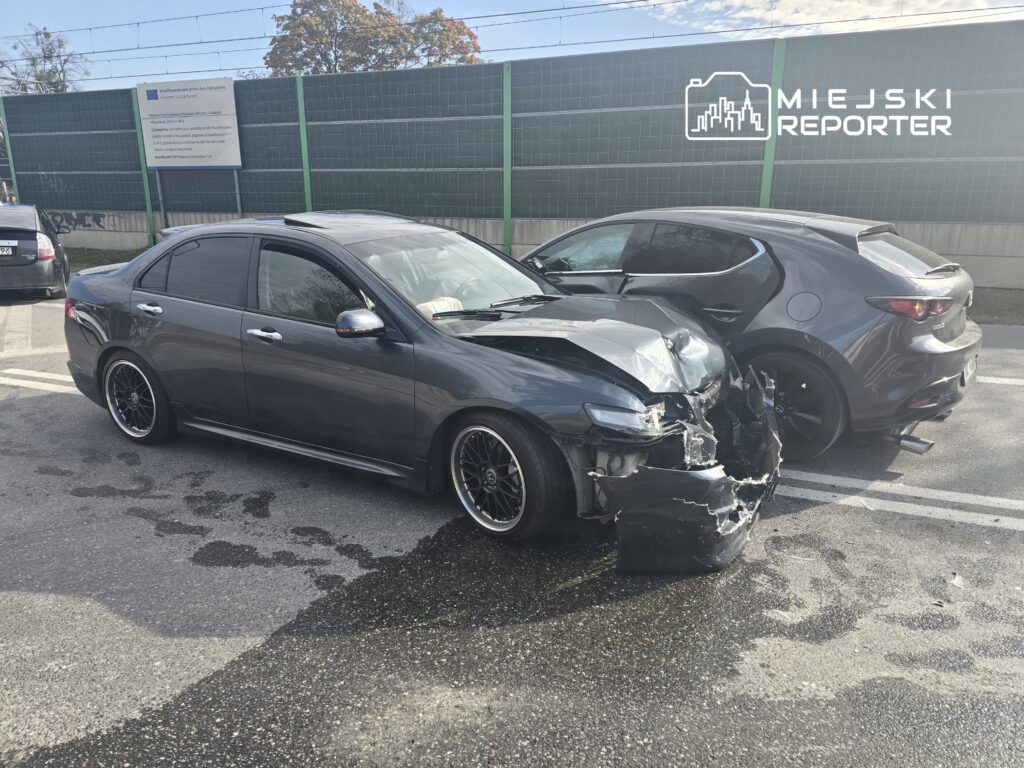 Dwa uszkodzone samochody na parkingu; szary sedan z rozdartym przodem i ciemny hatchback obok.
