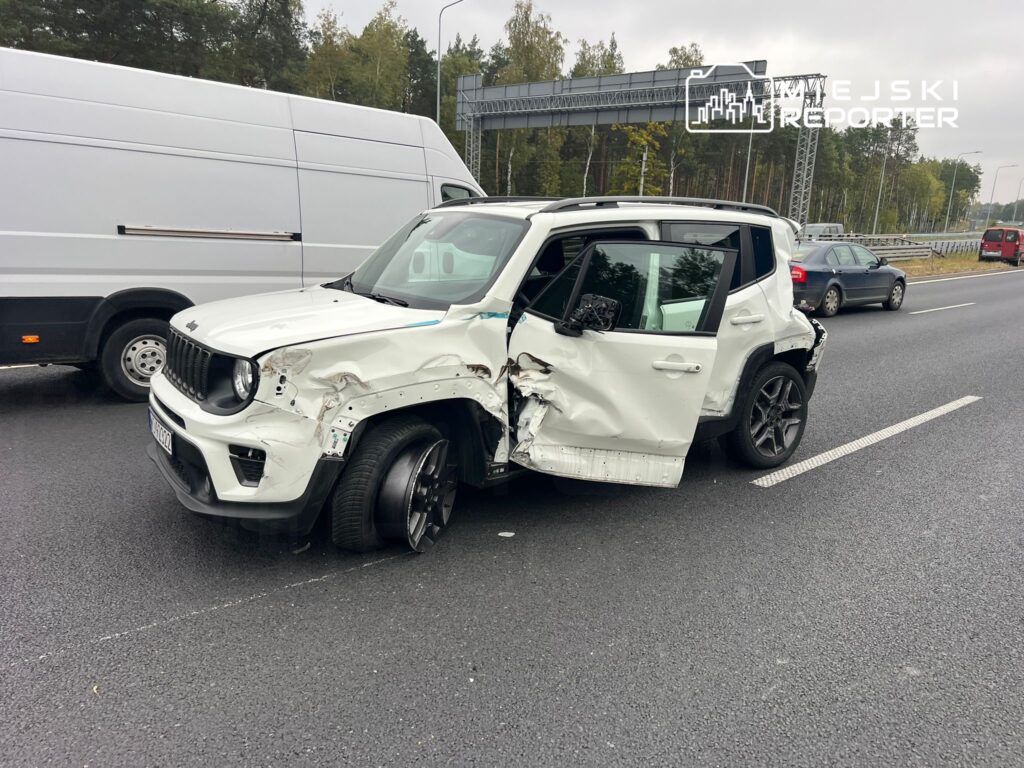 Uszkodzony biały SUV z wgniecioną boczną częścią stoi na jezdni obok dużego furgonu.