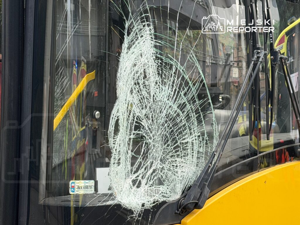 Zniszczona szyba frontowa autobusu z pęknięciami, znajdującego się na miejskiej ulicy.