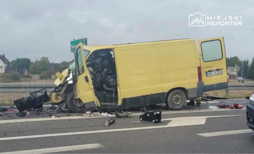 Zniszczona żółta furgonetka leży na poboczu drogi, a obok leżą rozrzucone przedmioty.