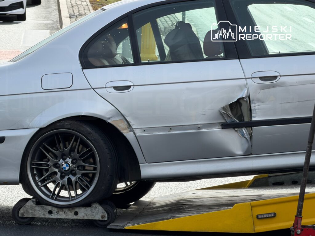 Uszkodzony samochód marki BMW z wgniecioną karoserią stoi na lawecie na ulicy.