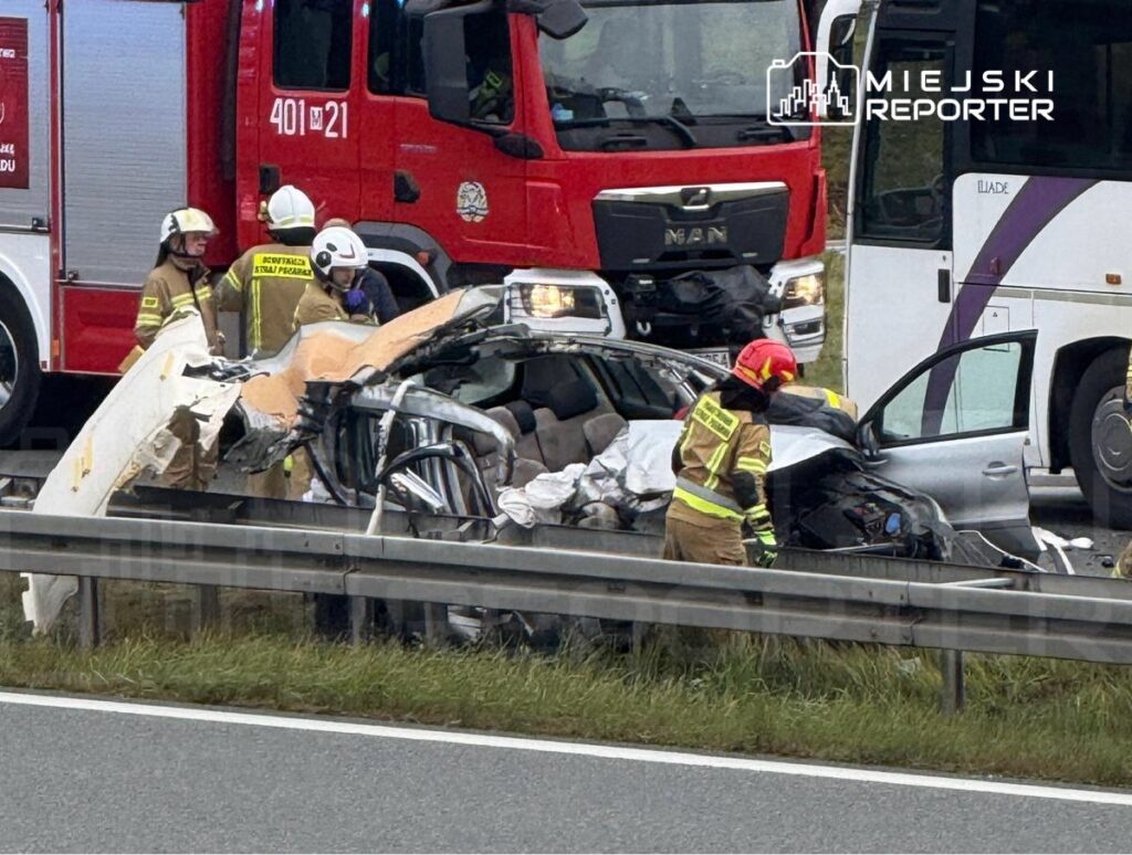 Strażacy udzielają pomocy poszkodowanym w wypadku drogowym na autostradzie, obok uszkodzonego pojazdu.